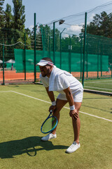 Tired african american sportsman with towel and tennis racket standing on court