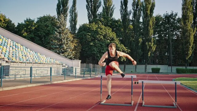 Young male athlete runs a distance overcoming obstacles at the city stadium. Obstacle course, professional sports, daily training