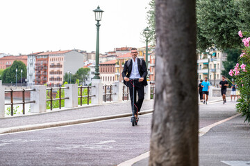 Young businessman in a suit riding an electric scooter while commuting to work in city. Ecological transportation concept