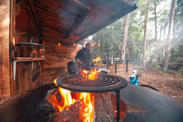 view of a professional outdoor barbecue restaurant with grill plate with flames in foreground and cook chef in background - obrazy, fototapety, plakaty
