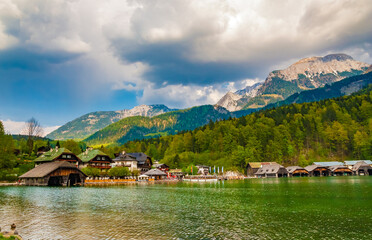 Fototapeta premium Lovely panoramic view of the village Schönau am Königssee with the alps in the background at the northern end of the Königssee lake in Bavaria, Germany. A boat is waiting at the pier.