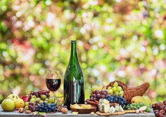 Grapes, bottle of wine and different cheeses on country wooden table and blurred colorful autumn...