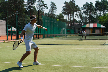Young sportsman playing tennis with blurred african american friend on court