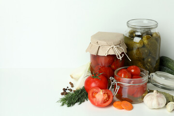 Jars of pickled vegetables and ingredients on white table