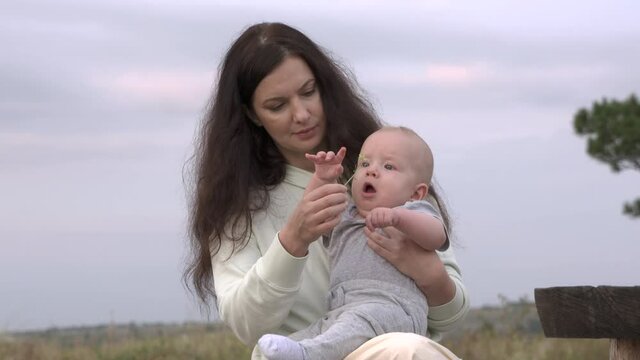 Portrait of caucasian mom with baby in her arms on a walk outdoors, mother lets her baby touch the plant, introducing him to the world around him. High quality 4k footage