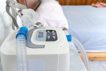 CPAP machine with air hose and head mask on bedside table