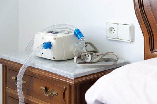 CPAP machine with air hose and head mask on bedside table