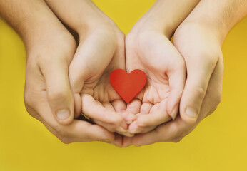 Young, loving people with a red heart in their palms. The hands of a man and a woman holding together a heart, a symbol of love, on a yellow background. The concept of Valentine's Day. Happy family