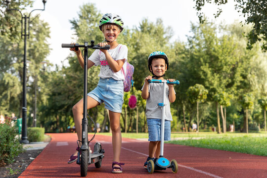 Portrait of two cute blond little caucasian sibling kids girl wear safety helmet enjoy having fun riding electric scooter city street park outdoors sunny day. Healthy sport children activity outside
