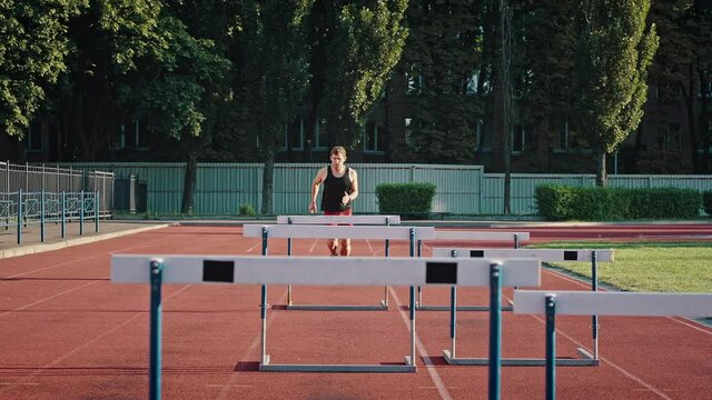 Professional athlete overcomes obstacles by jumping over them. Medium shot of a running track and field athlete at an outdoor urban stadium