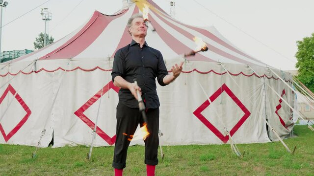 Male circus acrobat juggling with burning clubs