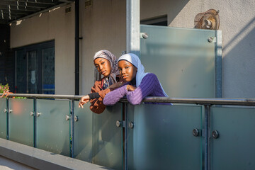 Portrait of two young women wearing hijabs leaning on balcony