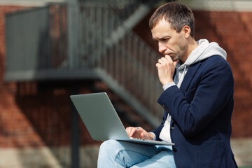 Concentrated businessman checking email on laptop, networking on project outdoors using 5g...