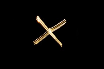 Drawn letter X with gold lights against black background. Light painting alphabet.