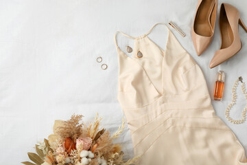 Stylish dress with elegant bijouterie, shoes and bouquet on white fabric, flat lay. Space for text