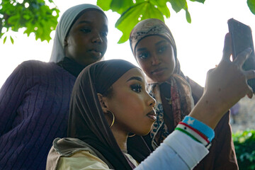 Three young women wearing hijabs taking selfie outdoors