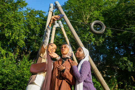 Three young women wearing hijabs taking selfie in park