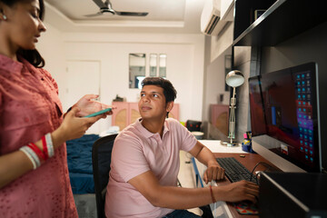 Young newlyweds talking while working from home in their living room.