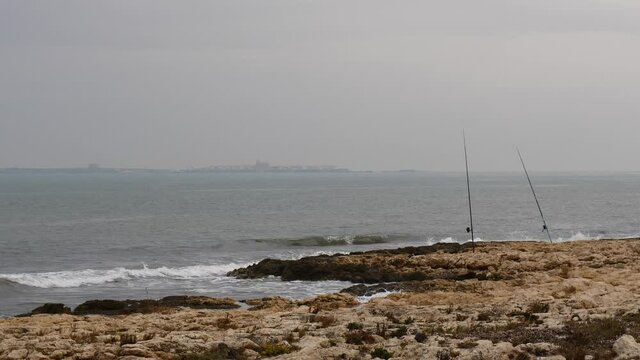 Fishing rod equipment on beach sea shore. Spanish coastline with Tabarca island on horizon.