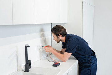 electrician checking power sockets with electric tester in kitchen