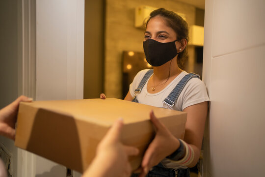 Young woman accepting delivery package at the doorstep with mask on her face.