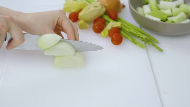 Hands cutting white onions on a white cutting board