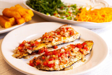 Grilled trout in tomato sauce with onion and pepper. In the background carrot, cabbage and pickle salad