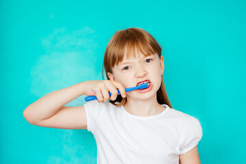 little child brushing teeth.  girl in a white t-shirt on a blue background. free space. dentistry for children.