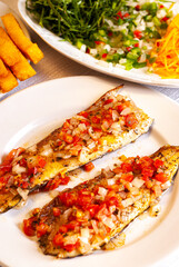 Grilled trout in tomato sauce with onion and pepper. In the background carrot, cabbage and pickle salad