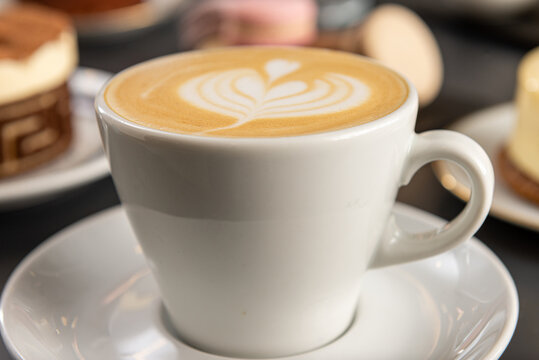 Primer plano de una taza blanca con cafe con diseño de arte latte con macarones de fondo con foco diferenciado
