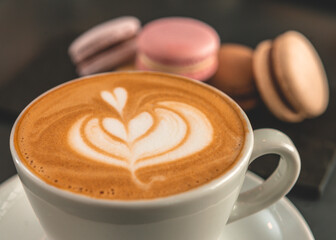 Taza de cafe con arte late en primer plano con macarones de fondo con foco diferenciado