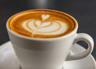 Taza blanco con cafe con diseño de arte latte en primer plano con foco diferenciado.