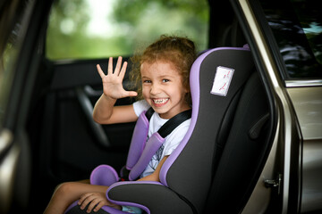 A liitle happy girl goes on a trip by car on a child safety seat summer vacation