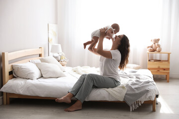 Fototapeta na wymiar Happy young mother with her cute baby on bed at home