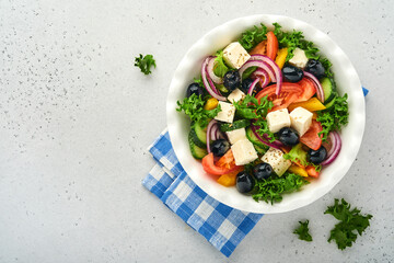 Traditional Greek salad of fresh cucumber, tomato, sweet pepper, lettuce, red onion, feta cheese and olives with olive oil on white plate. Healthy food, top view.