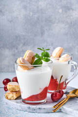 Summer cherry puff pastry with savoiardi cookies and cream cheese in glass on light grey background. Traditional tiramisu cake with fresh berries. Selective focus.