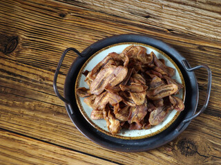 Plateful of keripik pisang or thin banana crisps or banana chips.  Typical Indonesian traditional snack. Sweet and crispy. Served on tray. Negative space available. Rustic wooden table as background.