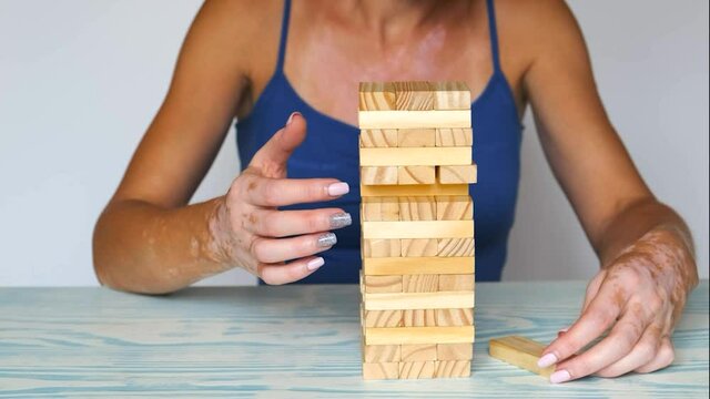 A woman with the skin disease vitiligo plays with wooden blocks in close-up. the tower is falling.