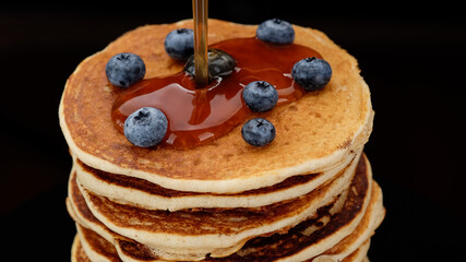 Pancakes with blueberry and maple syrup on black background. Pancake Maple syrup pouring onto stack of pancakes