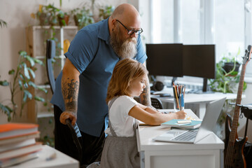 Bearded plump father stands looking at little girl doing hometask at home