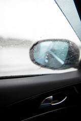 Raindrops on a side mirror and a side window while car running on the slippery high way with clear sky during a raining season. Random focus.