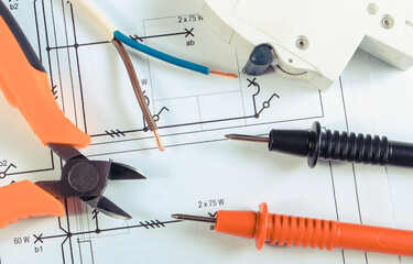 Cables of multimeter, pliers and electric fuse on construction drawing of house. Building home...