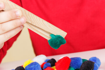 Preschooler playing with pompoms and wooden tongs. Development of kids motor skills, coordination and logical thinking