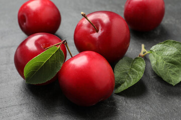 Delicious ripe cherry plums with leaves on black table, closeup