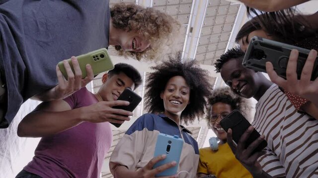 Low angle view of a group of young teenagers holding cell phones. Surprised faces looking at the screen. Concept of technology, connection, colorful.