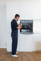 repairman in overalls fixing electric built-in oven in kitchen