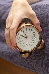 A woman's hand with an alarm clock hanging from the bed The concept of a difficult awakening an early rise.