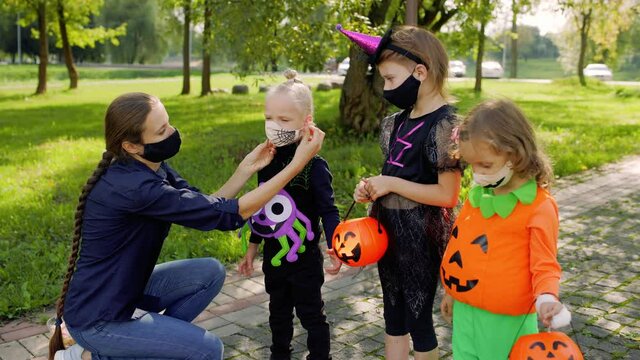 Mother putting protective face mask on her child during COVID-19 pandemic at Halloween. Kids trick or treat in Halloween costume and face mask. Children in dress up with candy bucket in coronavirus .