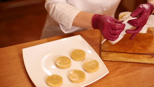 Professional confectioner in gloves puts a freezen pieces of buscuit on a plate