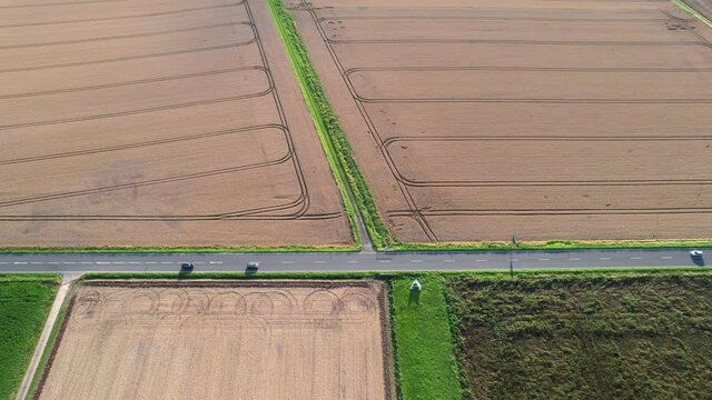Drone shot of a German country road with driving cars surrounded by agricultural land and fields. Aerial view from above. Transportation concept.
